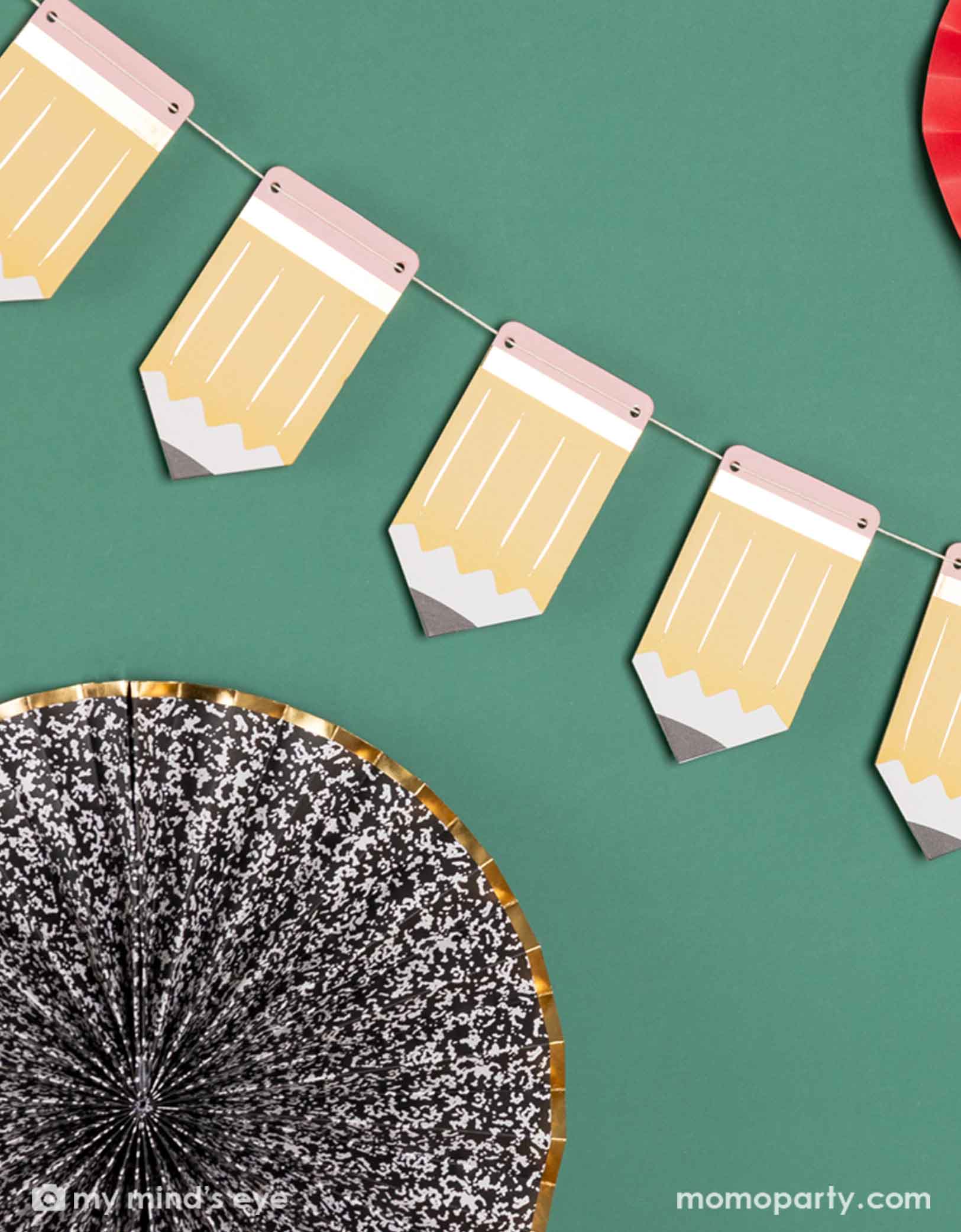 A green chalkboard decorated with the 5' pencil shaped party banner and apple, notebook shaped paper fans from Momopartys. A modern and easy decoration to celebration kid's back to school or first day of school special day.