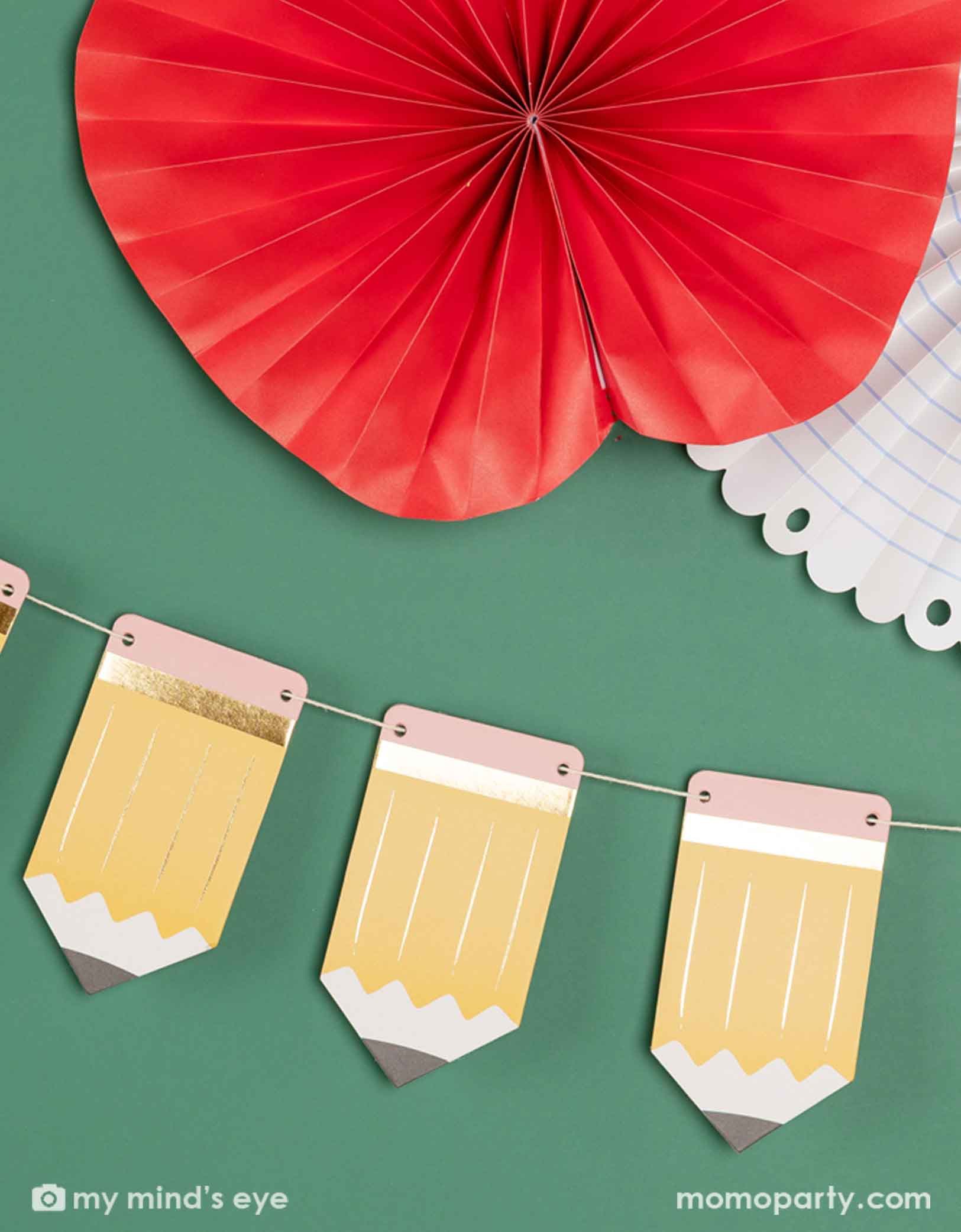 A green chalkboard decorated with the 5' pencil shaped party banner and apple, notebook shaped paper fans from Momopartys. A modern and easy decoration to celebration kid's back to school or first day of school special day.