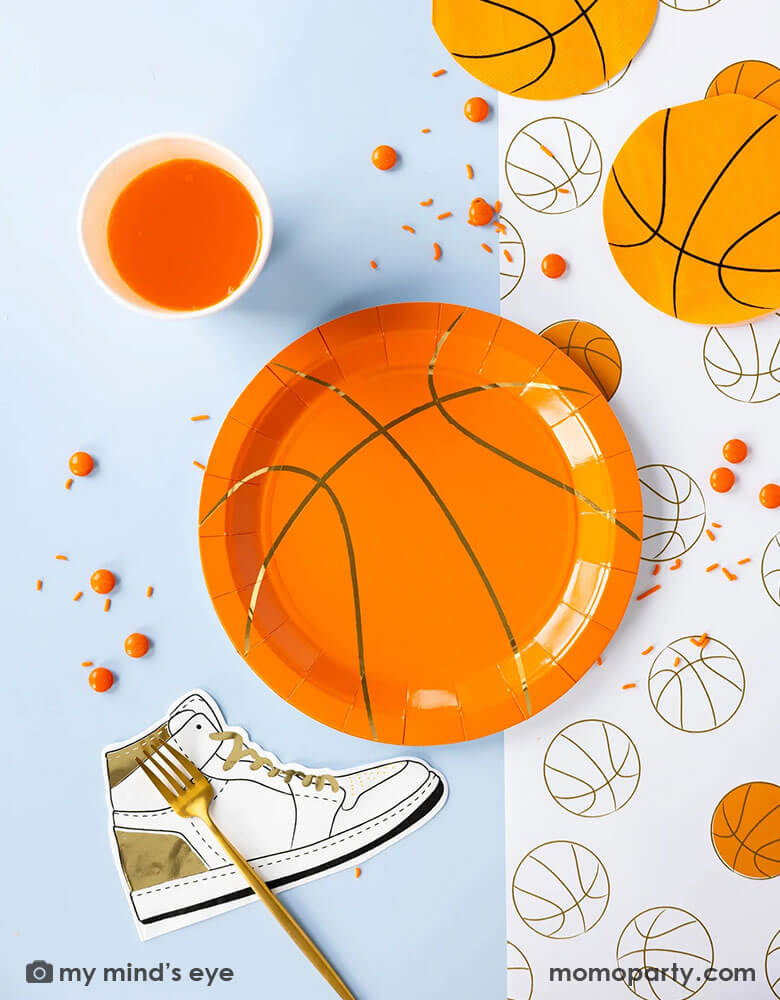 A basketball themed party table features Momopartys's basketball tableware by My Mind's Eye including basketball shaped plates & napkins, hightop sneakers shaped napkins, basketball net gold foil party cups and paper basketball table runner in gold foil details- a perfect table setting inspo for kid's basketball themed birthday parties or a fun NBA viewing party!