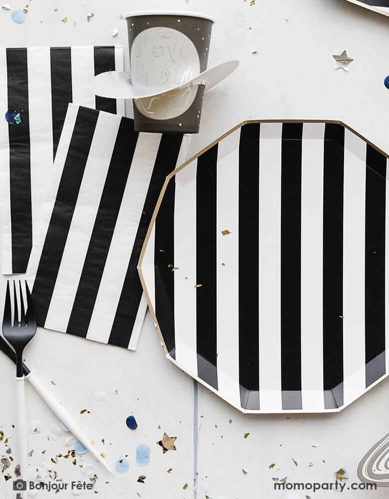 A space themed party table featuring Momopartys's Black Striped Party Supplies including paper dinner plates, guest towels, black and white cutlery set. With the planet 3D party cup and metallic star confetti around the table, this makes a perfect inspo for a chic, stylish and modern space themed celebration.