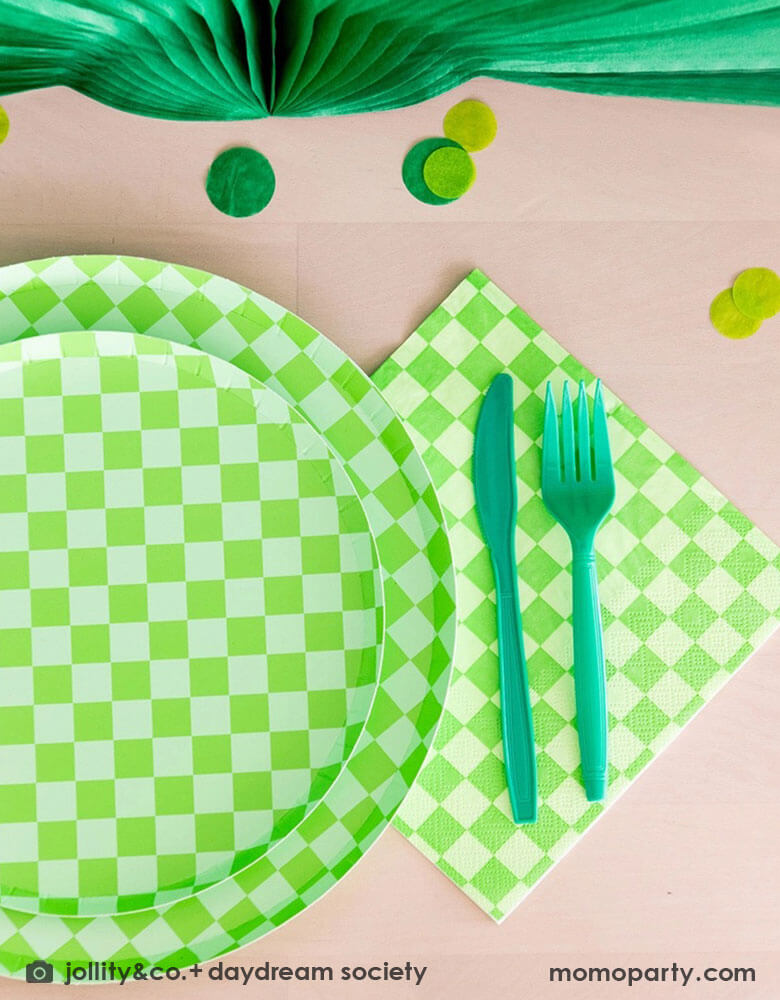 A green themed party table features Momopartys's Check it! Lime Green Checkered Tableware Collection by Jollity & Co. including 10" dinner plates, 8" dessert plates, 6.5" large napkins, green utensils and solid green party cups, with green paper fans as the centerpiece and large round green confetti scattered on the table.