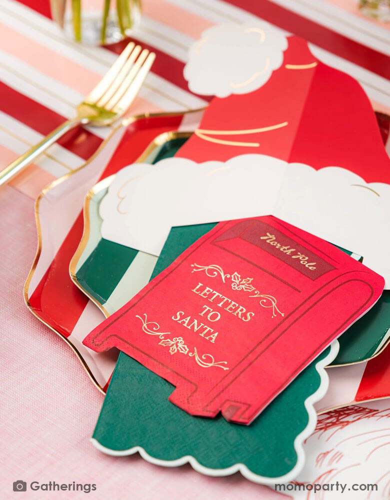 A festive Christmas party tablescape featuring Momopartys's Holiday red striped dinner plates and green side plates, along with a Santa hat shaped place card and a letter to Santa mail box shaped napkin, on a red and pink striped table runner. This makes a jolly table setting for this Holiday season.