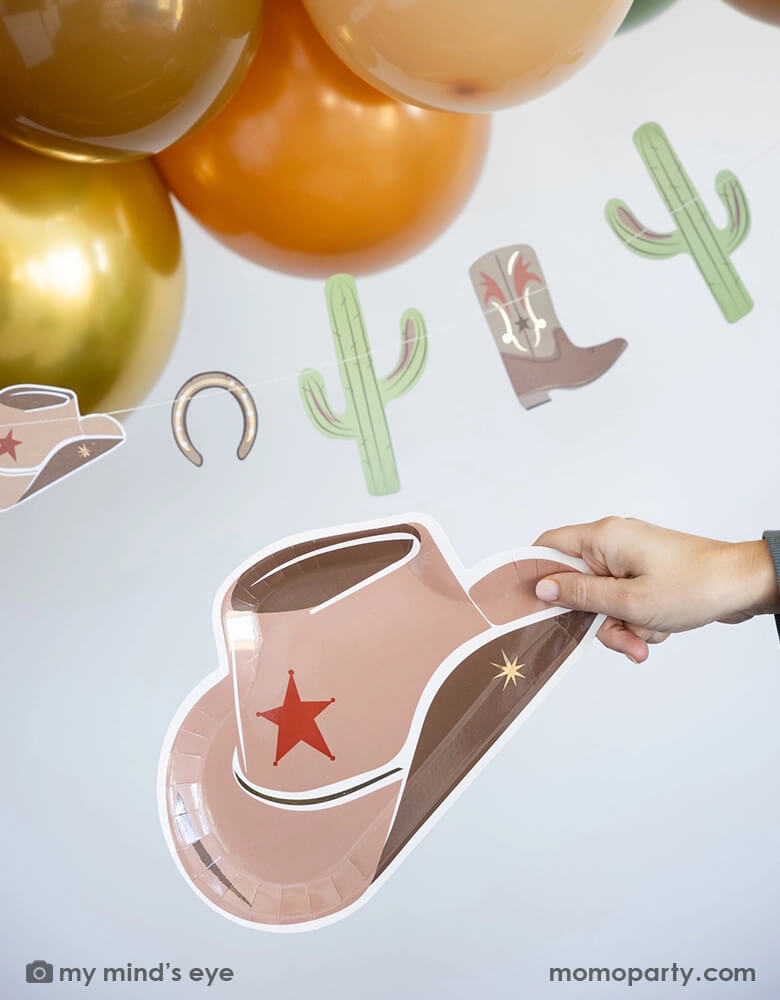 A cowboy Western themed party featuring Momopartys's cowboy themed party supplies including the Western themed party banner and cowboy hat shaped plate under some brown and gold colored balloon garland - a perfect decoration for a fun Western celebration or kid's First Rodeo cowboy themed first birthday.