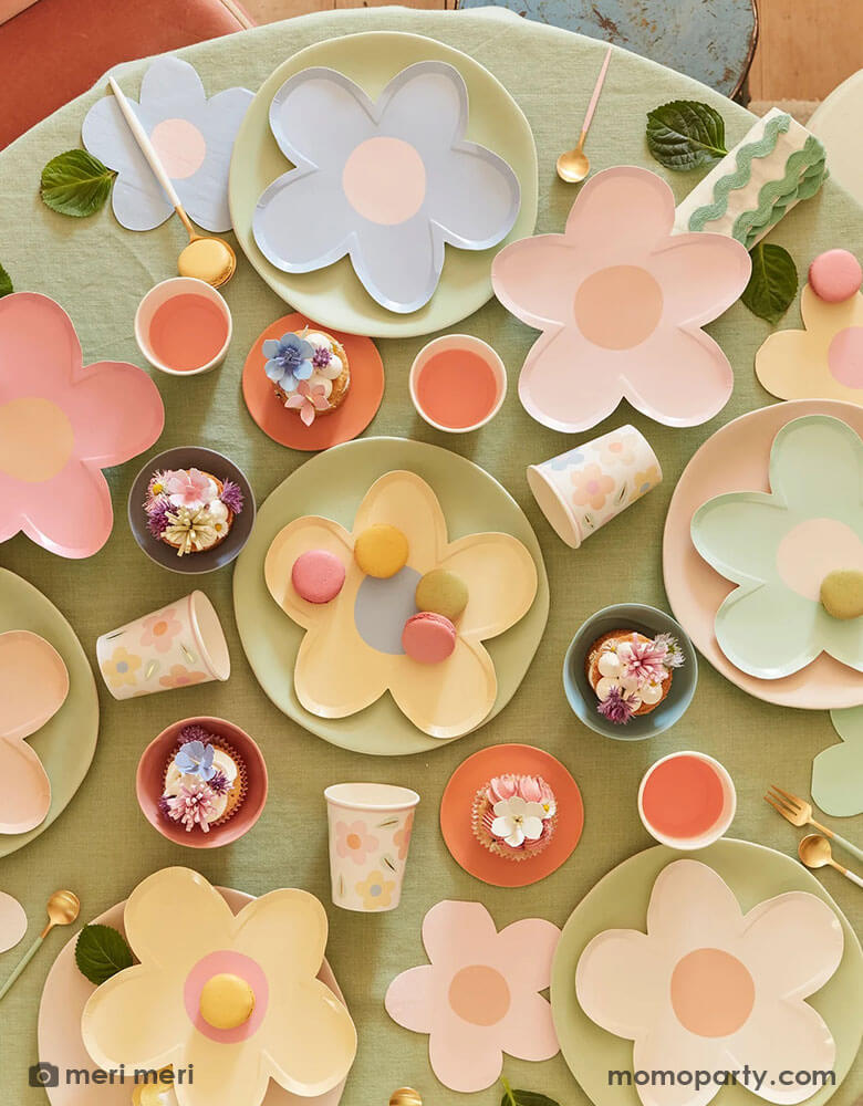 A round party table with adorable spring inspired treats and desserts featuring Momopartys's daisy shaped plates and napkins in multiple pastel colors, with pastel colored round plates underneath and happy flower party cups it makes a charming tablescape for a spring gathering, kid's daisy themed birthday or an Easter celebration.