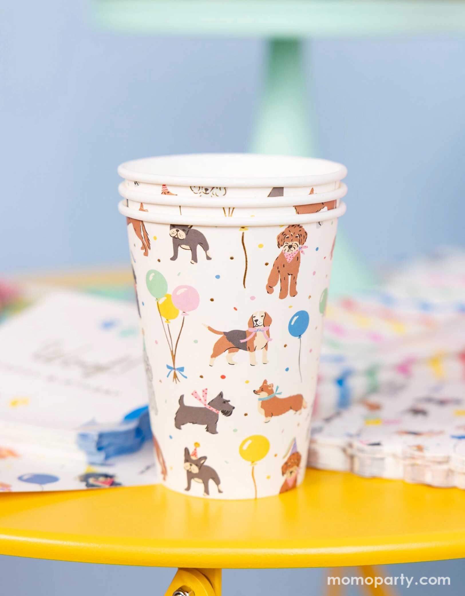 A festive and cheerful dog themed party table featuring Momopartys's dog party tableware collection including dog paper cups, napkins and party plates featuring adorable illustrations of different breeds of dogs with party hats, balloons and birthday cakes. This table is ready for a fun and playful birthday celebration for a pet lover!