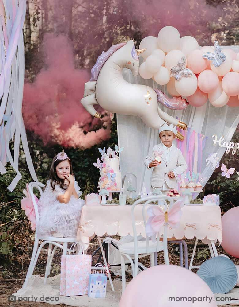 A magical set up for kid's unicorn themed birthday party featuring enchanting party supplies from Momopartys including unicorn themed party balloons, butterfly decorations, pink bow tablecloth, party bags, pastel colored party streamers and dreamy curtain backdrop, making this a whimsical inspiration for girl's birthday celebration.