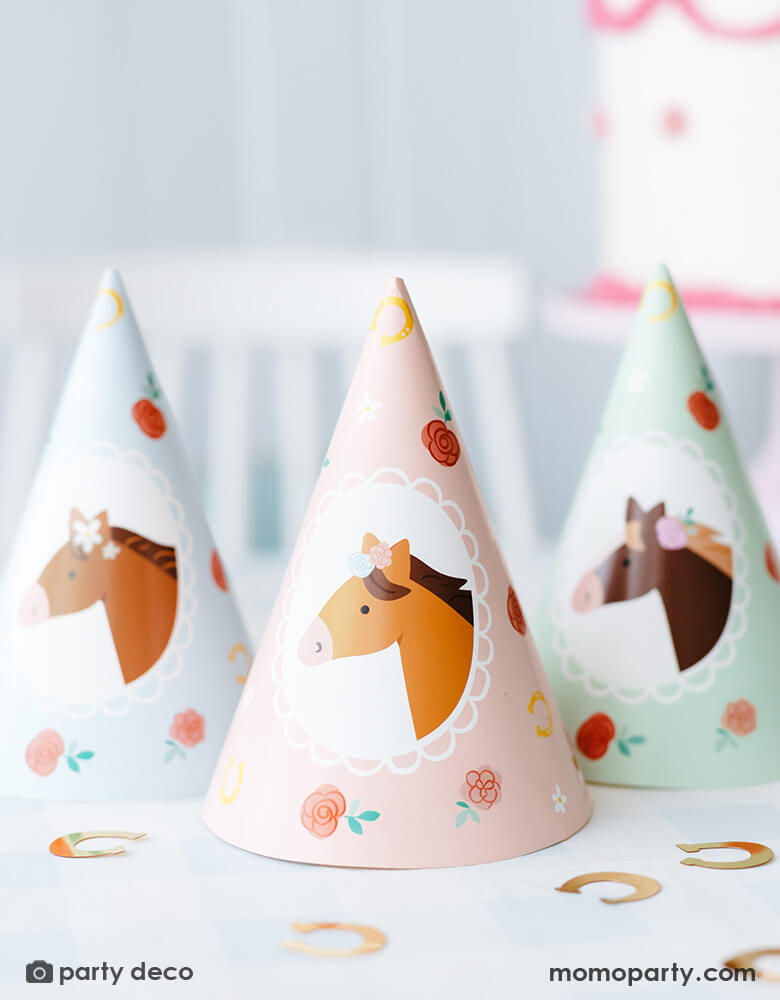 A close-up shot of Momopartys's floral pony birthday party hats by Party Deco in a horse themed party. On the table you can see gold horseshoe shaped confetti around the party hats which features adorable pony and floral designs in 3 different designs and colors of soft pastel pink, blue and green. Making this a darling addition to girl's pony themed birthday party.