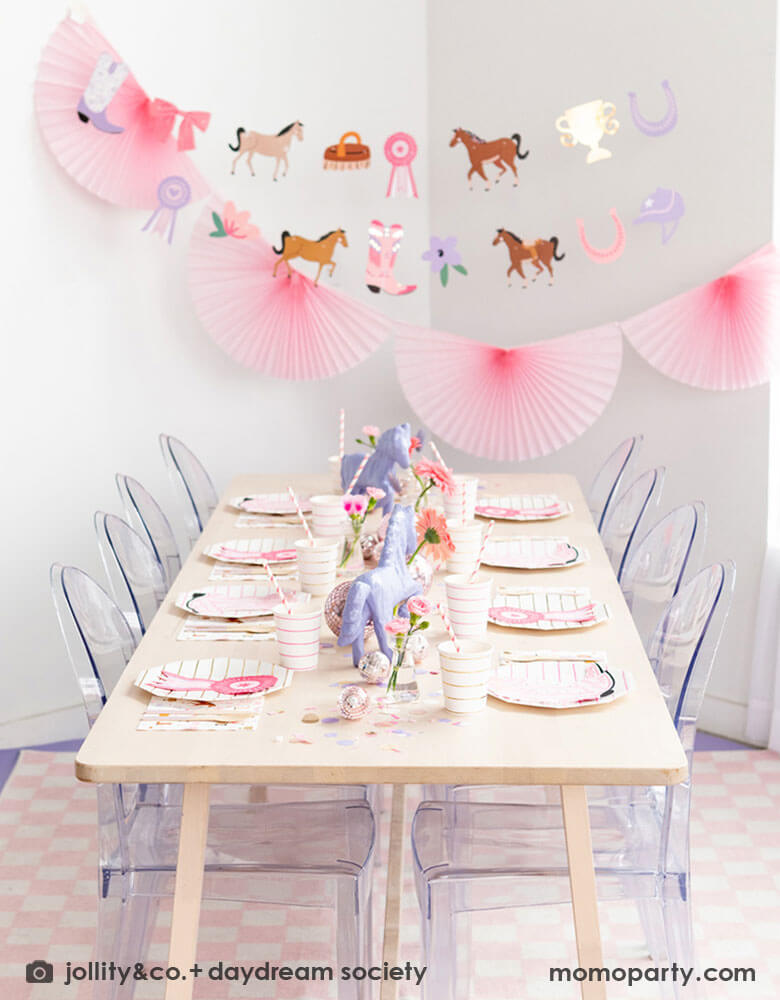 A girl's rodeo themed party decoration set up features Momopartys's cowgirl pony themed party supplies and decorations by Daydream Society including cowgirl boots shaped napkins, show ribbon shaped napkins, cowgirl rodeo themed paper napkins and pink striped paper plates and cups. With cowgirl themed party garland featuring paper pennants including ponies, show ribbons, pink horseshoes, bowes and flowers hung above the table, makes this a perfect inspiration for a girly rodeo themed celebration!