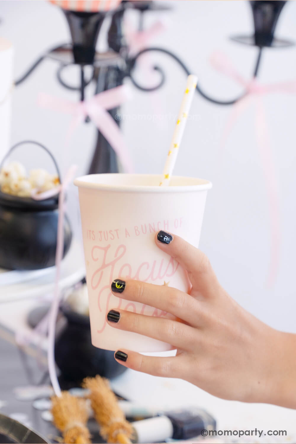 A kid's hand holding Momopartys's Hocus Pocus pink party cup in a witch themed Halloween party. The girl is wearing black nail polish with Halloween themed nail stickers from the Snails Nail Polish Halloween Spooky Pack - which makes a perfect party favor or activity for kid's Halloween party.