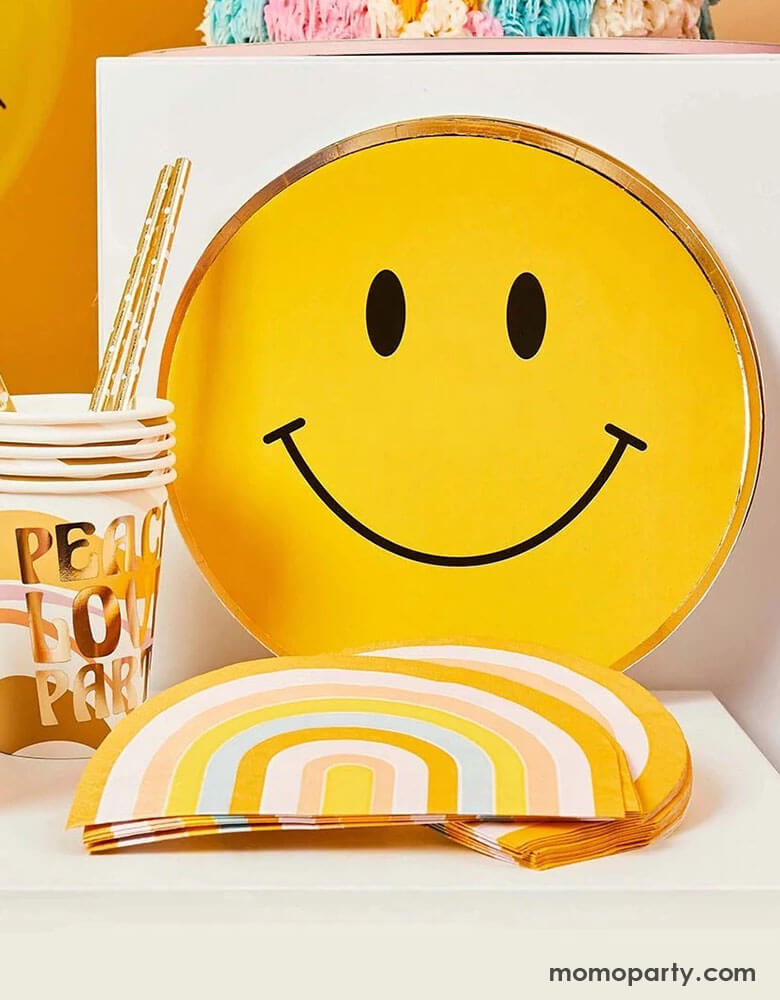 A display of Momopartys's 9" Smiley Gold Foiled Paper Plates, Peace and love retro party cups, and retro rainbow shaped napkins by Hooty Balloo. This cheery collection in the warm, retro color is perfect for any happy celebration or groovy hippie vibes themed parties.