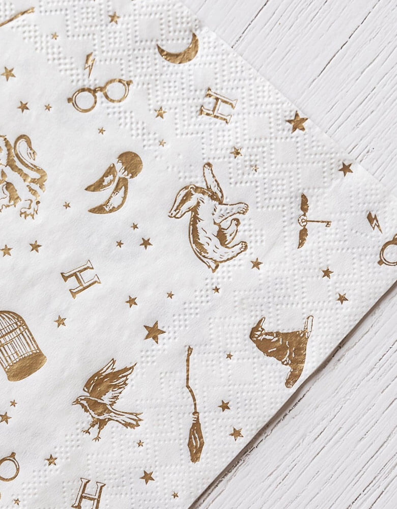 A close up shot of Momopartys's 6.5" x 6.5" Harry Potter Large Napkins by Bonjour Fete. Comes in a set of 24 napkins with elements including glasses, wizard hats, moons, stars and owls from Harry Potter in gold accent. Throw a magical bash with these Harry Potter party napkins. With whimsical gold accents, this modern design is perfect for any wizarding event.