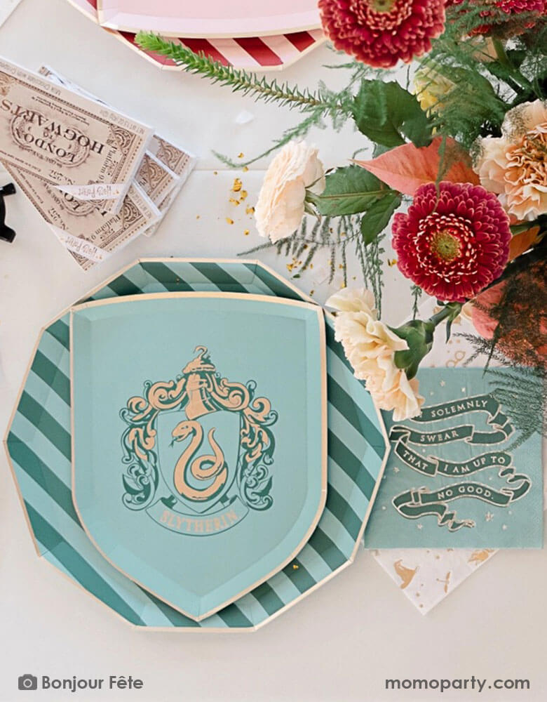 A beautiful and elegant Harry Potter themed party tablescape features Momopartys's Harry Potter house pride shield-shaped 7" side plate with Slytherin logo and color paired with 10.25 green striped dinner plate. Next to the plates are Harry Potter motif large napkins in gold foil and Slytherin green small napkins. On the table are some tickets Hogwarts and pretty flower arrangement - making this a great inspo for a modern Harry Potter themed birthday party celebration.