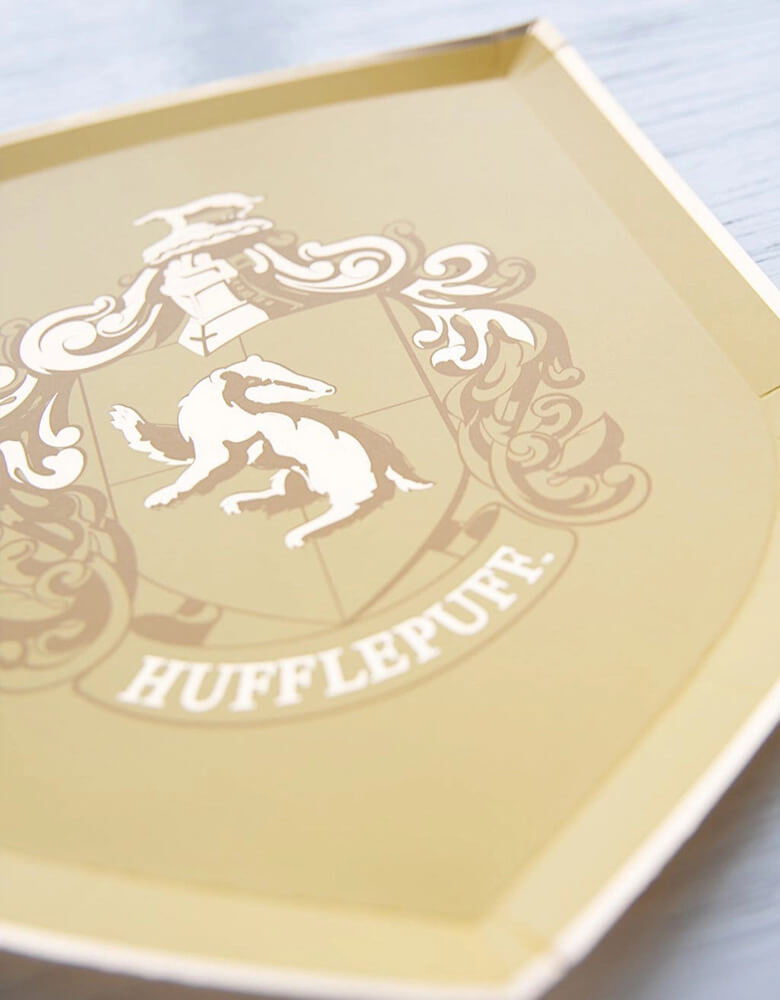 A close up shot of Momopartys's 7" Harry Potter House Pride Small Plates by Bonjour Fete. Comes in a set of 8 shield-shaped paper plates in 4 colors/designs each represent the color and symbol of the houses including Hufflepuff, Gryffindor, Slytherin and Ravenclaw. These plates are prefect for your Harry Potter themed celebration, be it a birthday party, a Halloween bash or a magic themed gathering.