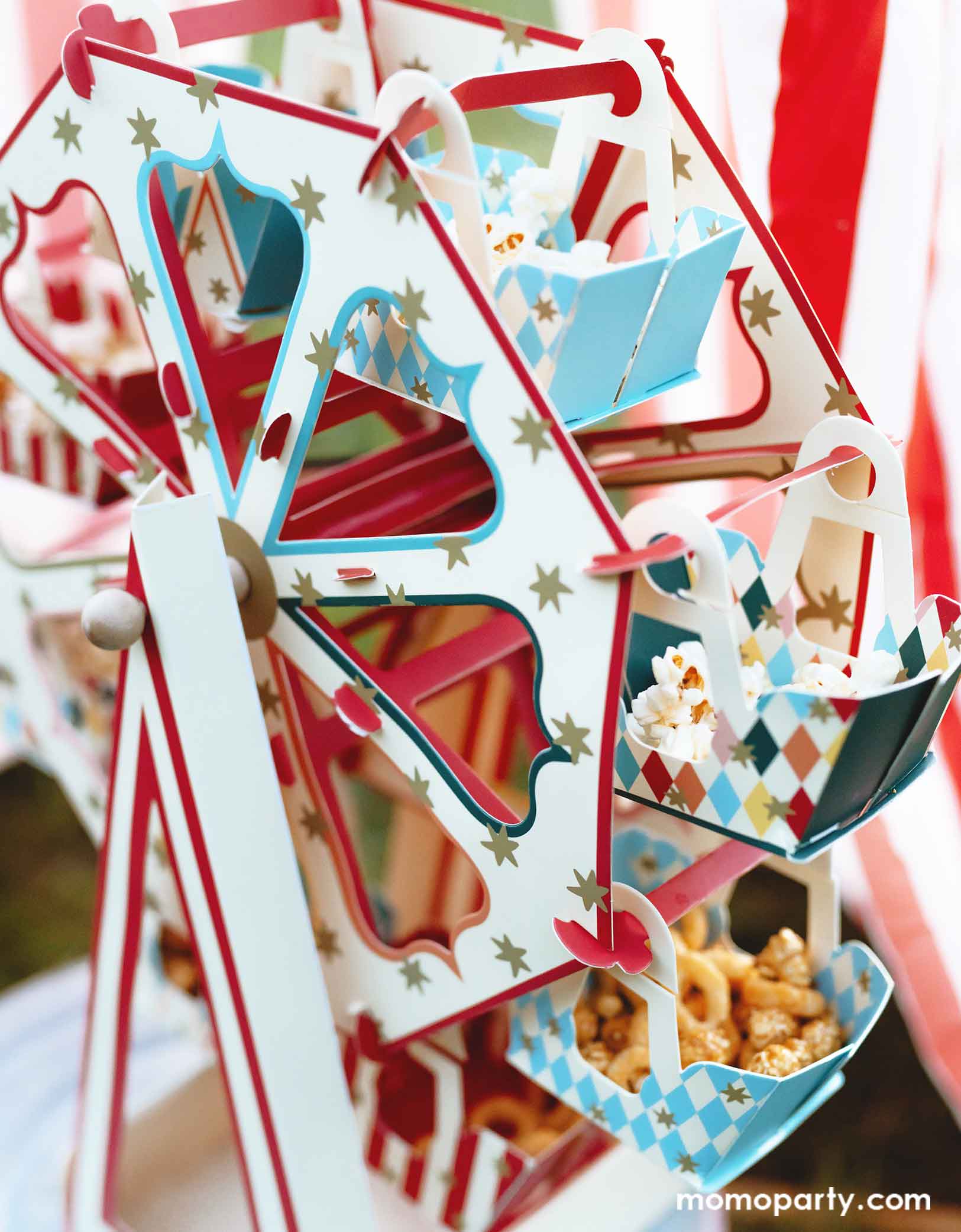 A close up shot of Momopartys's 18.9" x 19.7" Carnival Ferris Wheel Snack Stand by Party Deco. This stunning centerpiece with its circus-inspired design is loaded with treats and cupcakes and they kids are grabbing the goodies from this fun treat stand.