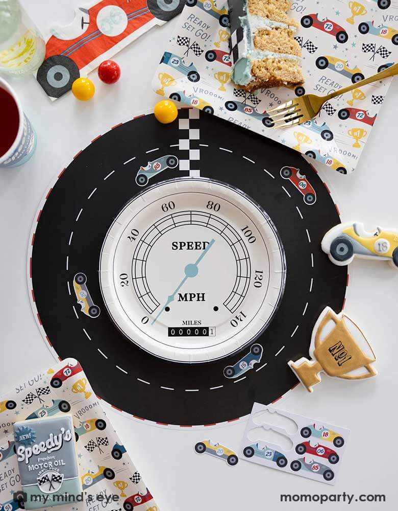 A fun race car themed party table place set featuring adorable race car themed party supplies from Momopartys including a race track placemats adorned with interactive race car stickers in the middle of the placemat is a speedometer shaped plate. Around the tableset laid some race car themed sugar cookies in matching colors and designs around the race car pattern square plates by My Mind's Eye. A perfect inspo for kid's race car themed party tablesetting ideas.