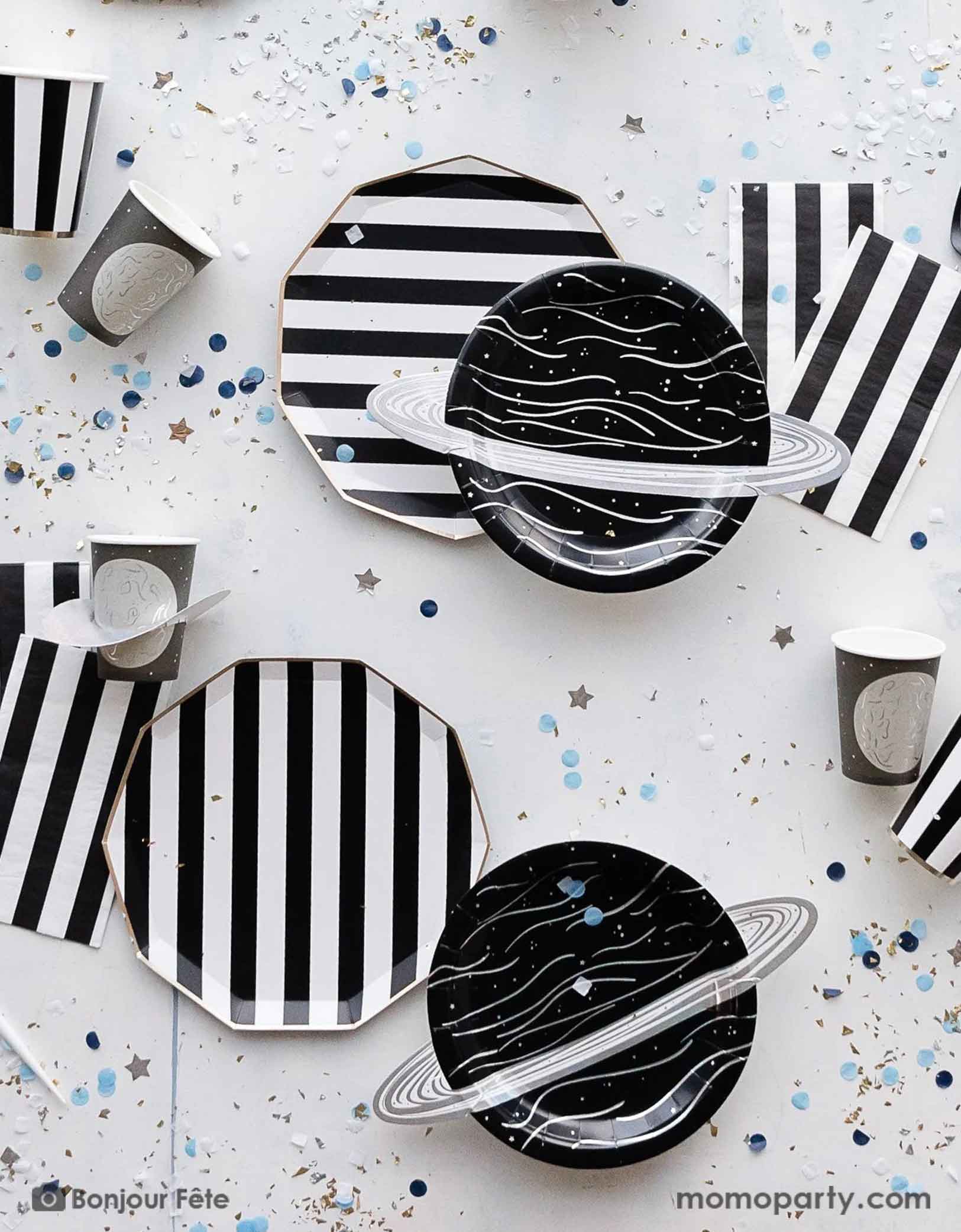 A space themed party table featuring Momopartys's Black Striped Party Supplies including paper dinner plates, guest towels, black and white cutlery set. With the planet 3D party cup, planet shaped plates and metallic star confetti around the table, this makes a perfect inspo for a chic, stylish and modern space themed celebration.