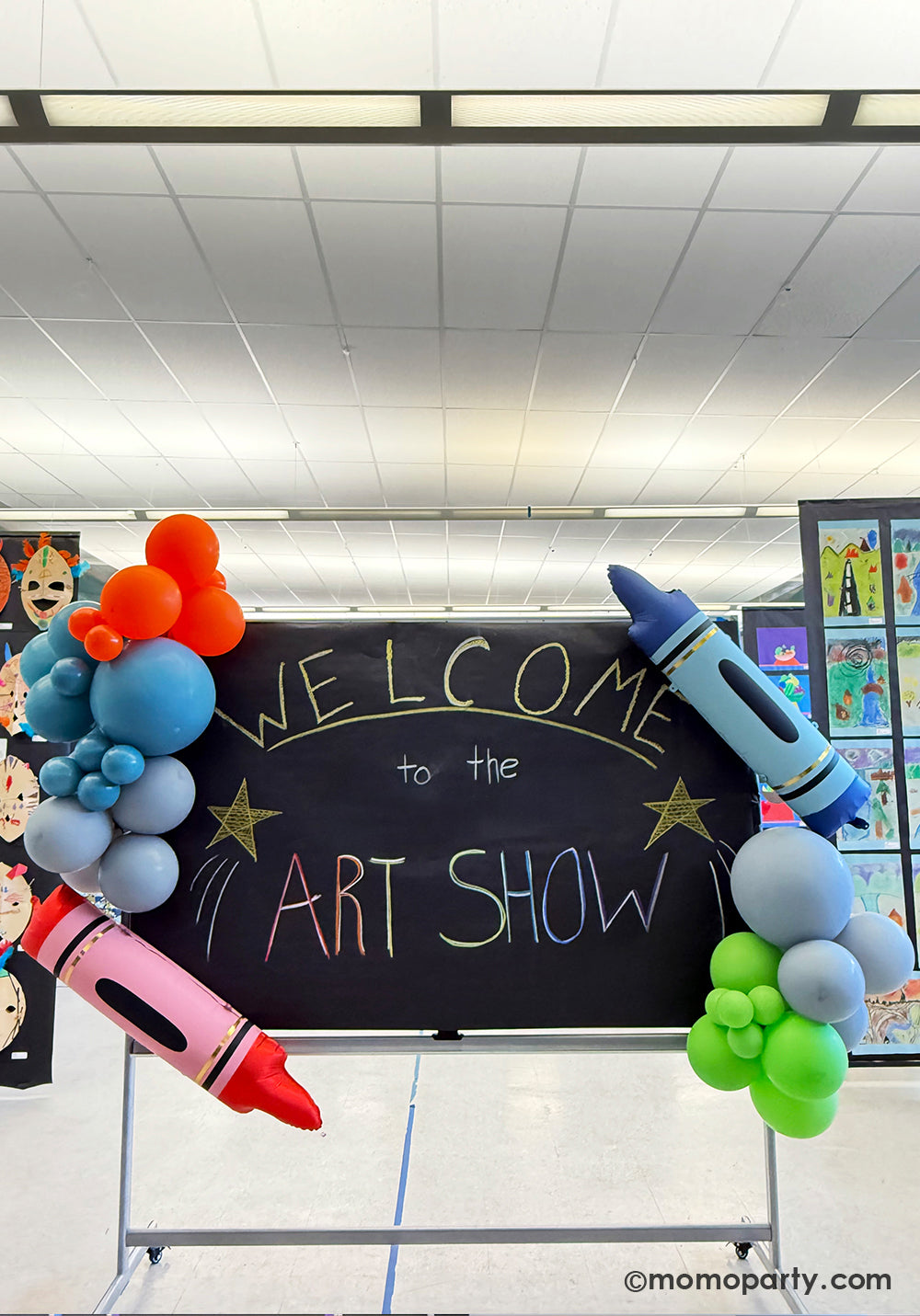 A school chalkboard decorated with a festive and colorful balloon garland along with Momopartys's 40" x 9" blue & red crayon shaped foil balloons at a kid's art show in a school event. This easy balloon installation with bright color and fun design is also perfect for kid's school themed celebration, be it a back to school party, a first day of school celebration or any kids event at school.