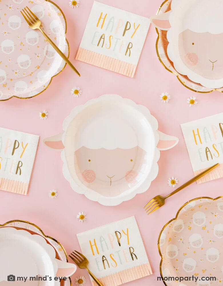 A table-setting featuring Momopartys's 9" x 9" lamb head shaped plates in adorable water color design by My Mind's Eye. Around the plates are pink scatter lamb scalloped plates and Happy Easter pink fringe napkins. With daisy flower confetti and gold forks, it creates a darling vibe for a kid's friendly Easter tablescape.