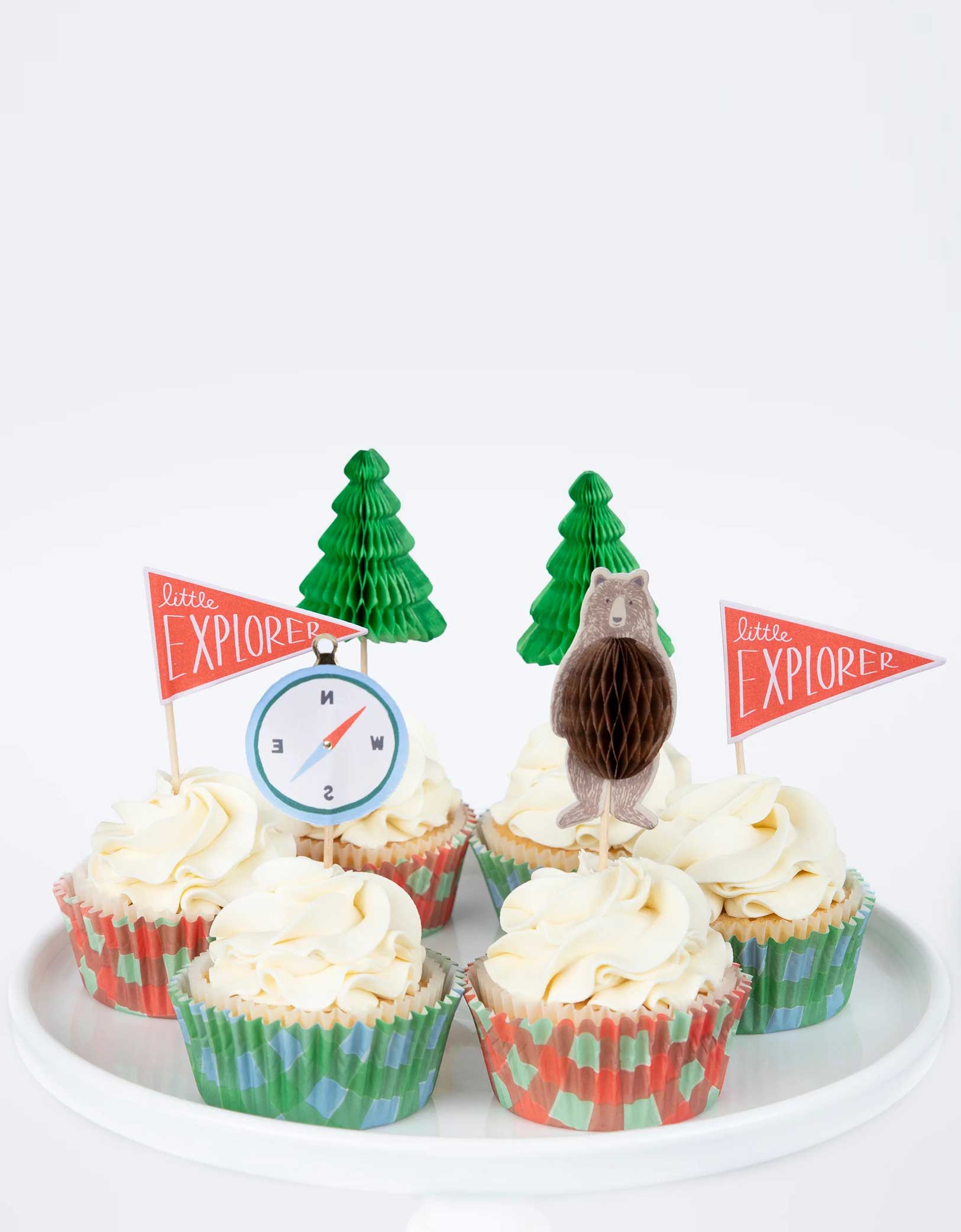 A few cupcakes decorated with Momopartys's Camping Adventure Cupcake Kit by Meri Meri. Create a cupcake centerpiece for your camping adventure party, or hand them out to hungry little explorers as a sweet treat. This kit is beautifully presented in a camper van style box. 24 cupcake toppers in 4 designs, including honeycomb bears, honeycomb trees, compasses and explorer flags, with shiny gold foil details.