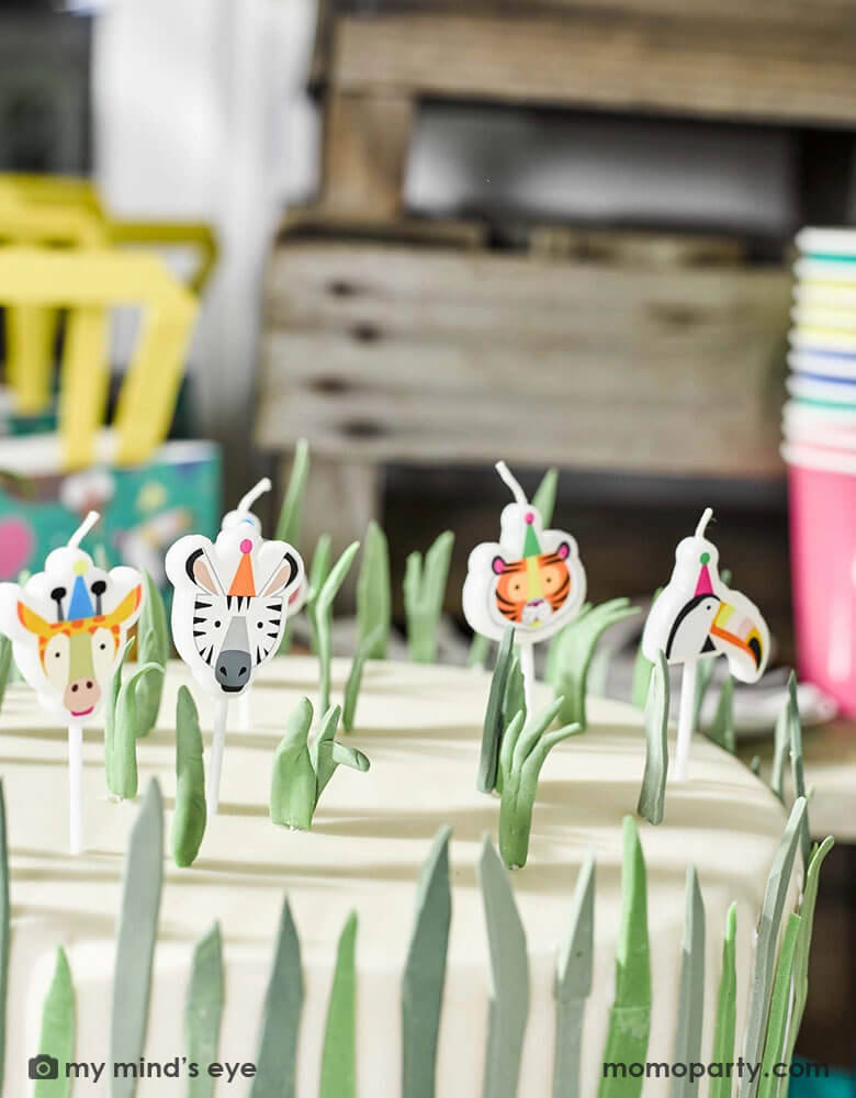 A jungle themed birthday cake topped with Momopartys's animal birthday candles of a tiger, a zebra, a monkey, a toucan and a giraffe by Talking Tables.