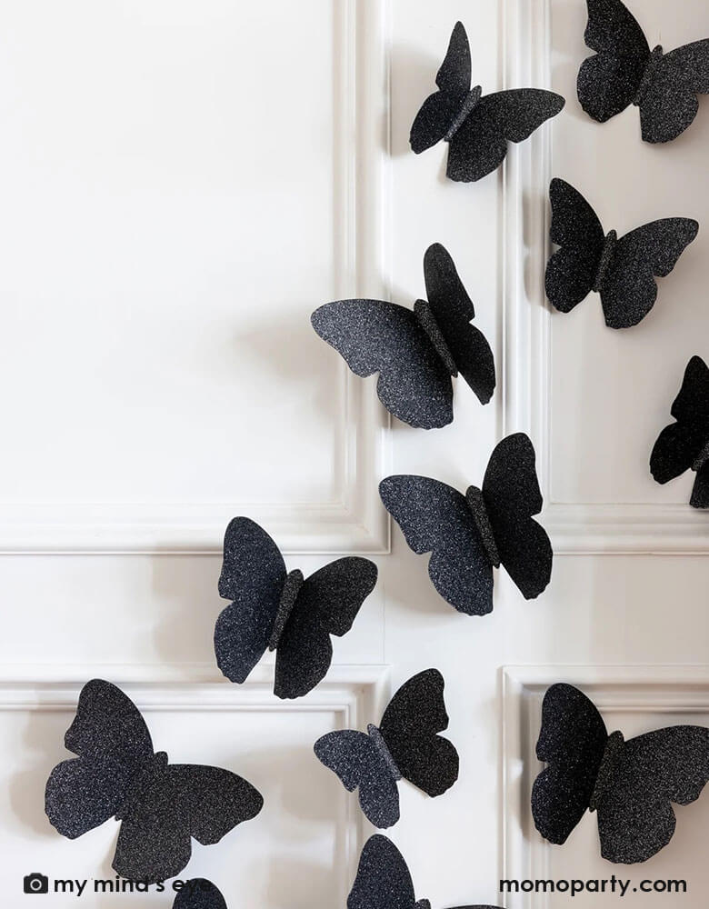 A close up of a white wall decorated with Momopartys's black glitter butterfly wall decorations by My Mind's Eye.