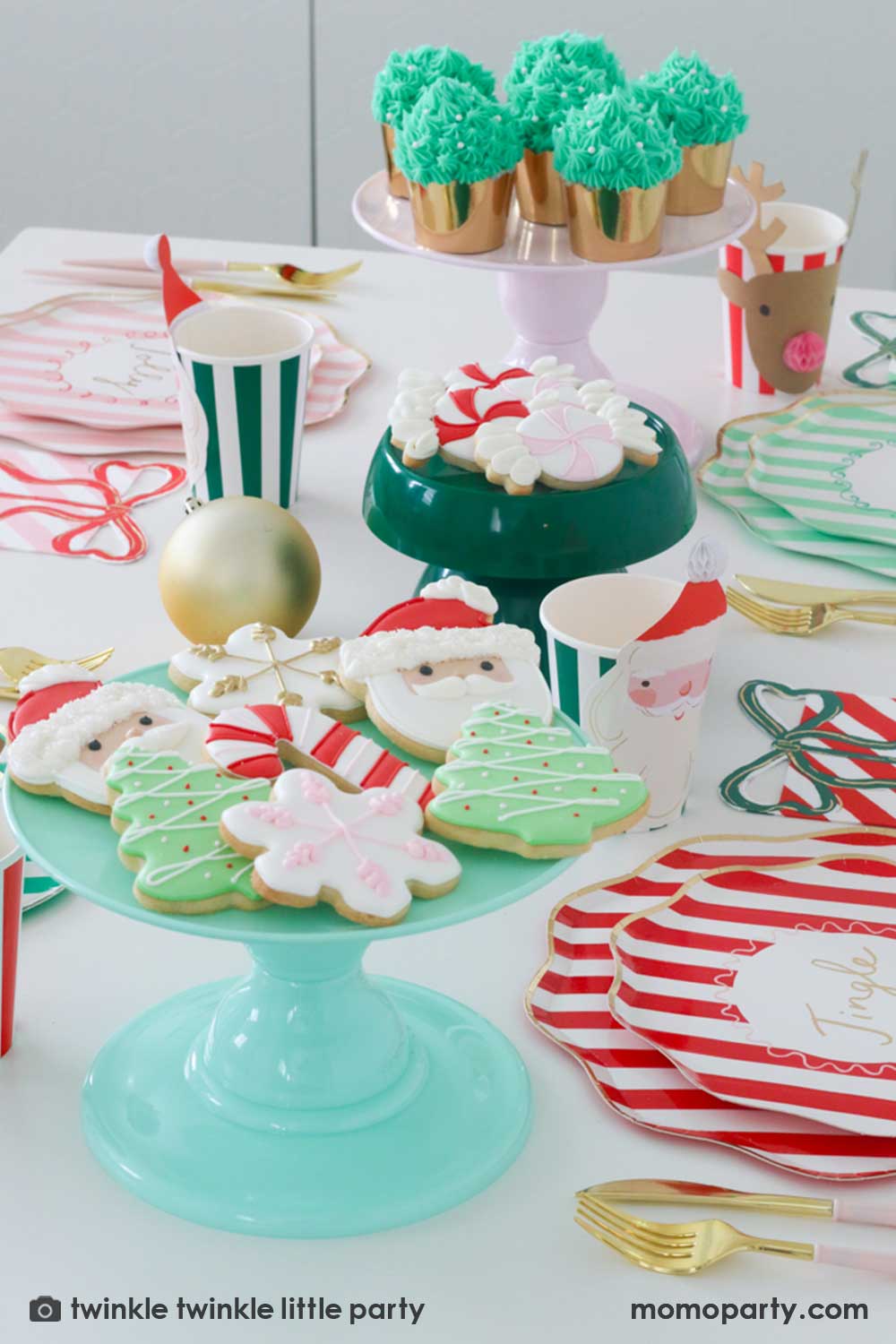 A festive Christmas party table featuring Momopartys's Festive striped dinner plates, side plates, present with a bow shaped napkins and Christmas honeycomb party cups in Santa design by Meri Meri. In the center of the table are a mint and green cake stand with festive Holiday cookies in the design of Peppermint, Santa, Christmas tree, candy cane and snowflake. Makes this a modern inspo for a festive Holiday table setting.