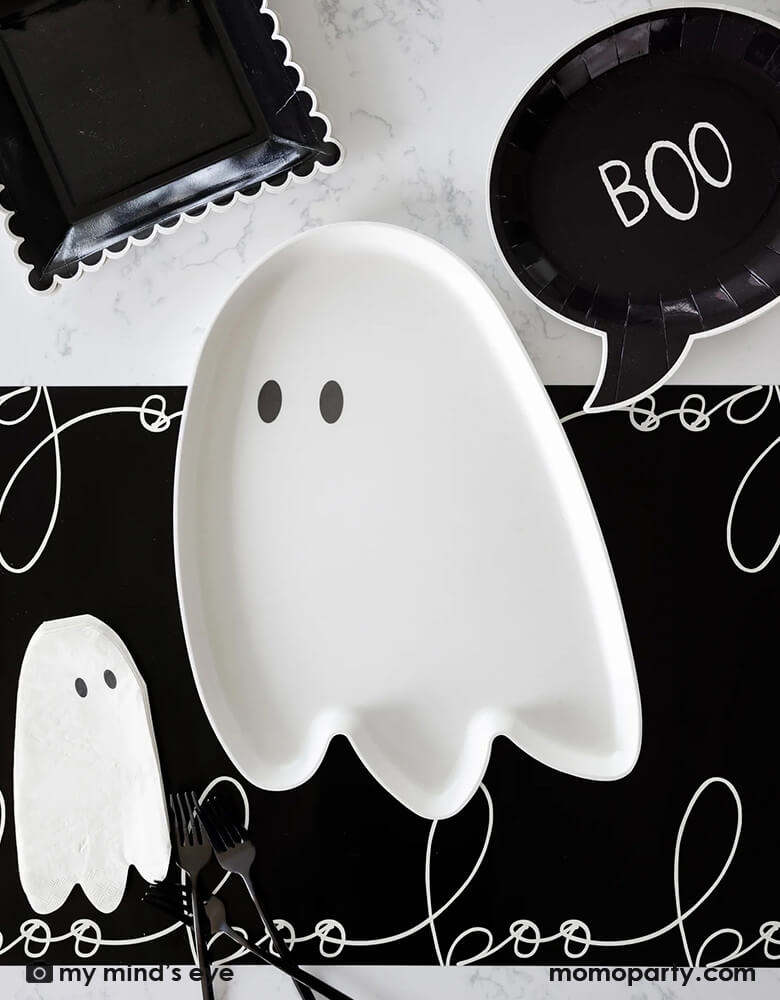 A black and white Halloween table featuring Momopartys's 12" x 16" ghost shaped bamboo reusable tray. Around it it's the black boo shaped plates, ghost shaped napkins on a black table runner with "boo" scripted font written over it. All makes a cool and spooky ideas for a kid's Halloween bash, trick or treat party, or Halloween theme birthday party table setting inspiration.