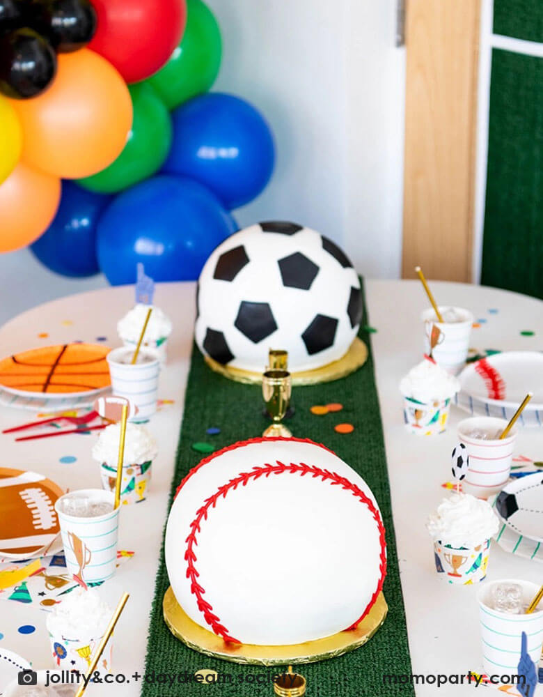A fun sports themed party table filled with Momopartys's sports themed party tableware including soccer ball, football, baseball, basketball shaped plates, football shaped plates, basketball shaped plates with mint and red striped plates and cups, plus some good sport large napkins featuring bright colors and fun illustrations of sports elements. In the center of the table there's a faux grass table runner and baseball shaped birthday cake, all makes great inspirations for kid's sport themed parties.