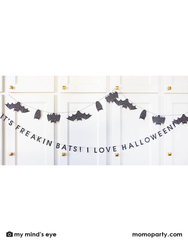 A white cabinet set decorated with Momopartys's 6' Freakin' Bats Garland by My Mind's Eye. This banner set includes a spooky stitched bat banner and a stitched word banner featuring the phrase "It's freakin bats! I love Halloween." These banners create a frightfully fun scene and sure to drive your guests batty this Halloween.