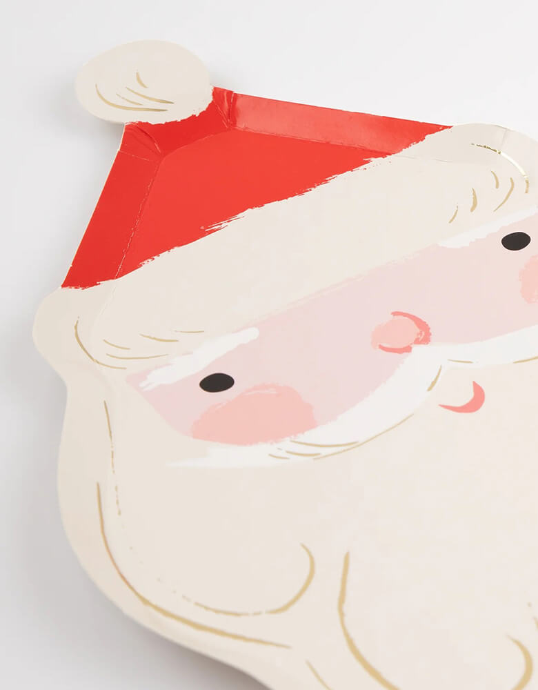A close up shot of Momopartys's 7.25 x 11.5 inches Jolly Santa shaped plates by Meri Meri. For a festive party table guaranteed to delight your guests smile, look no further than these Santa plates. It doesn't get more traditional than this jolly fellow, and the red and gold colors will team beautifully with all your Christmas tableware.