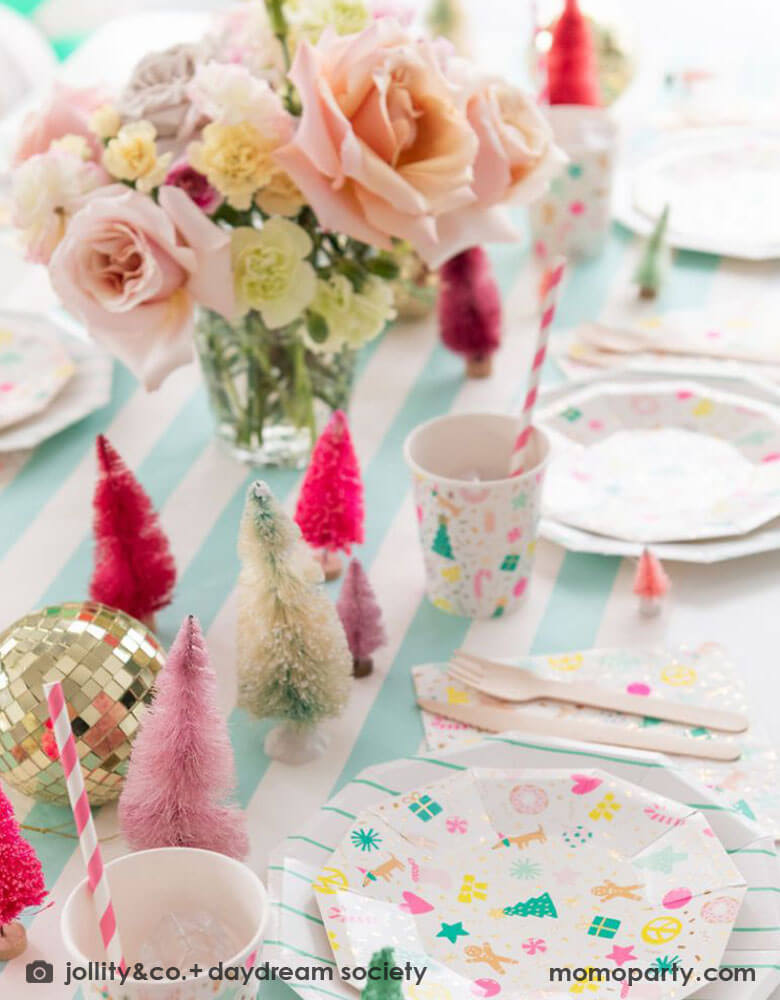 A festive Christmas tableset featuring Momopartys's Merry and Bright tableware collection by Daydream Society. The Christmas themed plates, cups, and napkins on a mint striped table cover which adorned with bottle brush Christmas trees in different shades of pink and a gold disco ball. With the floral centerpiece, it makes a great inspo for a festive party table setting this Holiday season.