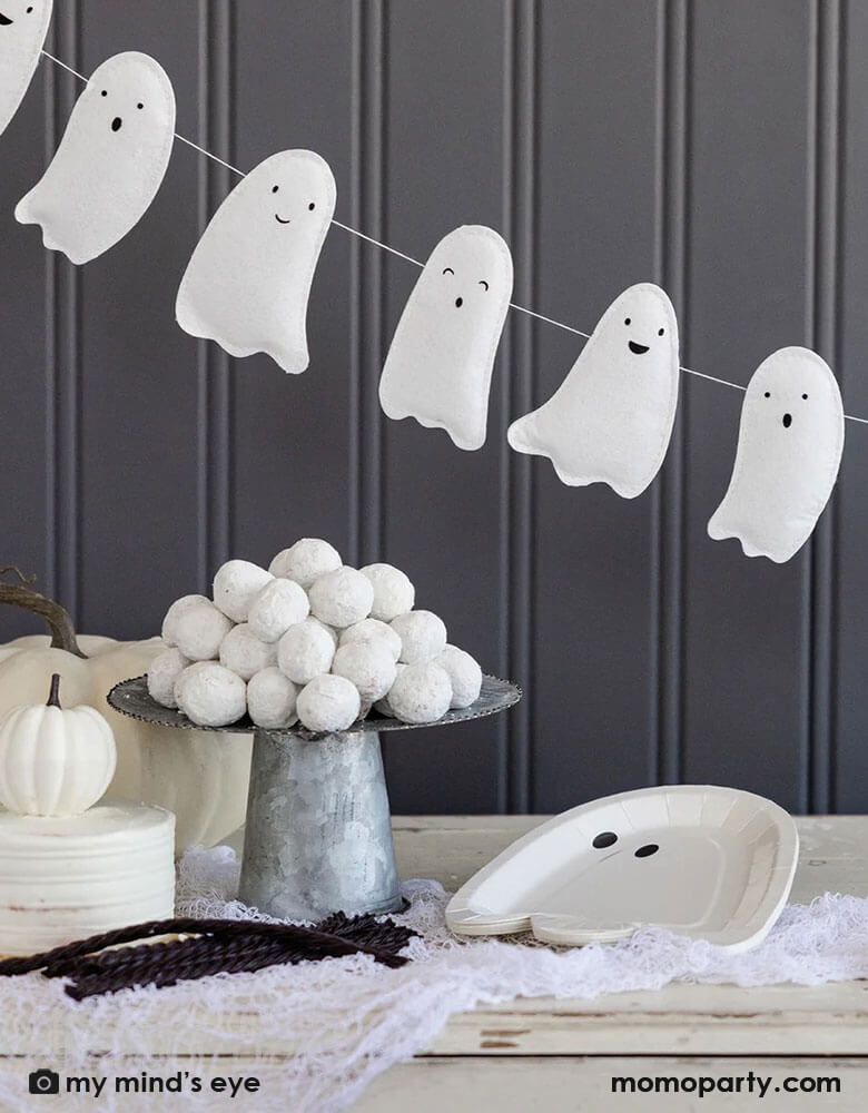 A gray farmhouse wall decorated with Momopartys's 6f puffy ghost shaped banner in front of a dessert table which is filled with Momopartys's 10" x 7" ghost shaped plates by My Mind's Eye, a bowl of white donut holes, and some white pumpkins around. Makes it a simply yet cute Halloween home decoration inspiration.
