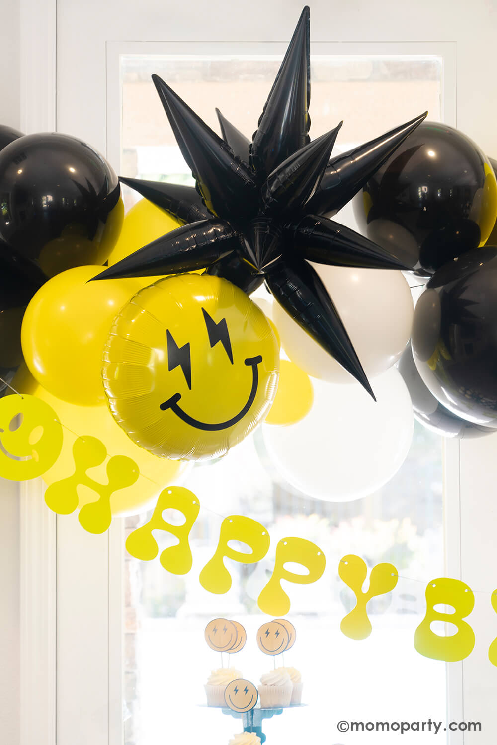A close-up look at Momopartys's 'Cool Dude' themed Birthday Party. Featuring a captivating balloon garland in black, white, and yellow, accented by a black starburst foil balloon and a smiley face foil balloon with lightning bolt eyes. This stylish decor is complemented by a retro neon happy birthday banner. Perfect for a boy's 'One Happy Dude' themed first birthday, a 'Two Cool' themed second birthday party, 'Ten Rad Years' 10th birthday celebration, or kids birthday party for all ages.