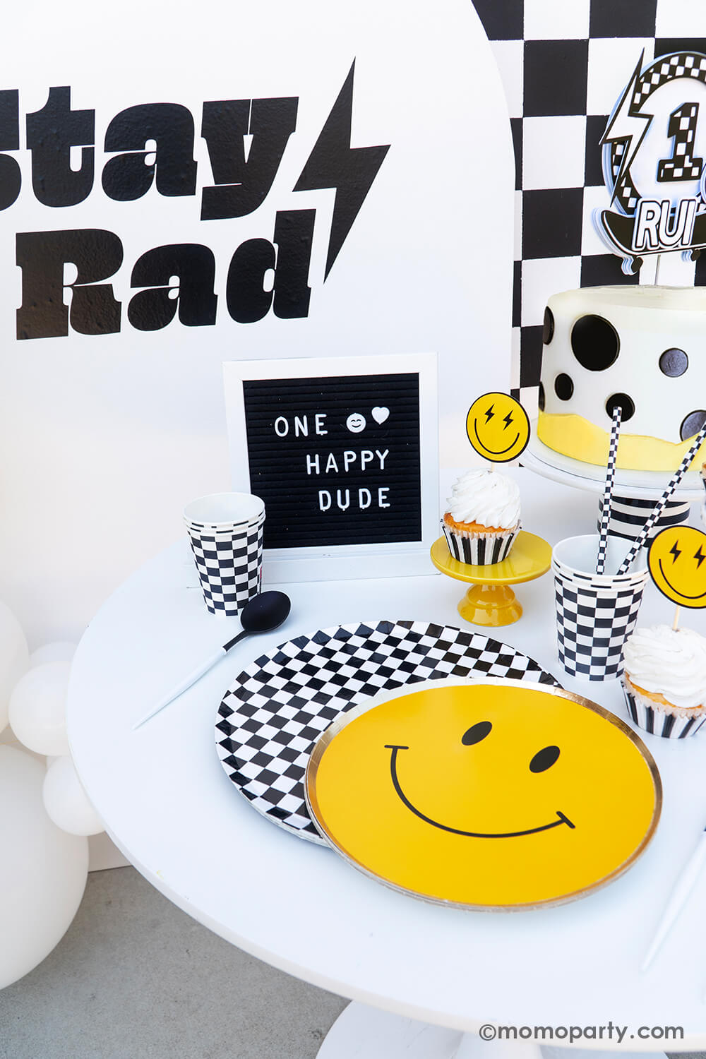 Baby boy's "One Happy Dude" first birthday party tablescape by Momopartys. Featuring the classic black and white checkered patterned plates, cups, napkins and smiley face plates, this rad party table decoration is perfect for your little cool dude's very first big day! With a mix of cool dude aesthetics, smiley-face accents, and checkered patterns in black and white, we've got the perfect recipe for a memorable boy's birthday bash. Don't miss out on making this party as special as your little boy.