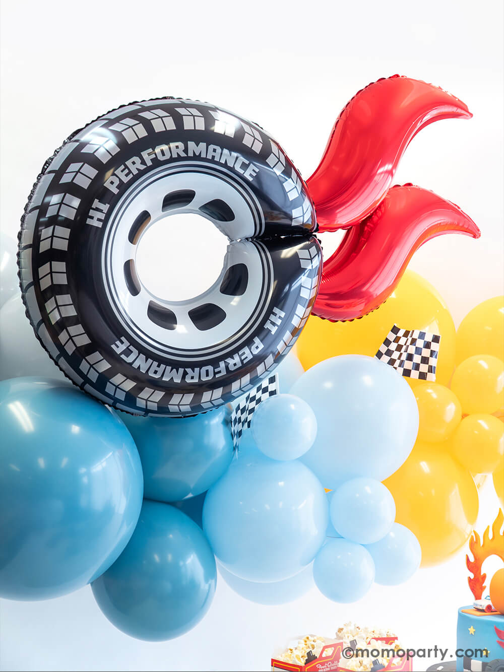 A close up of Momopartys's Hot Wheels themed balloon decoration featuring an organic balloon garland in orange and blue, and a wheel shaped foil balloon with red curve balloons attached as flame. On the balloon cloud there are some race car checkered flags adorned, making this a perfect decoration backdrop idea for kid's Hot Wheels themed race car birthday party.