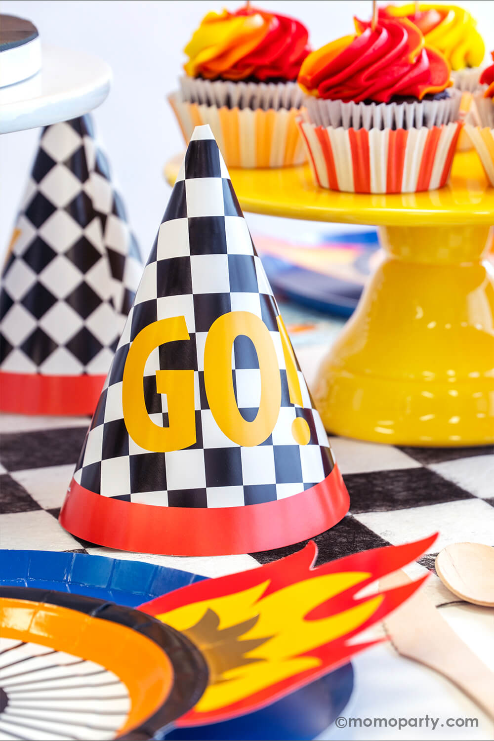 Momopartys checkred GO! birthday hats next to red and yellow swirl cupcakes in a Hot Wheels themed birthday party where there's wheel shaped plates with flame on them along with midnight blue dinner plates.