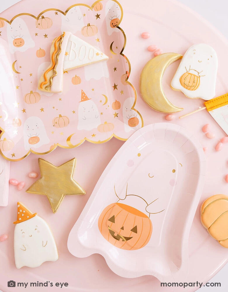 A pink table filled with pink Halloween ghost themed party supplies from Momopartys including the pink ghost shaped paper plates with a jack-o-lantern, the 10" x 10" pink ghost scattered scalloped dinner plates, and a Boo felt party pennant. With matching ghost themed sugar cookies around and pink candies, it's a great inspo for a kid's friendly pink Halloween party this spooky season!