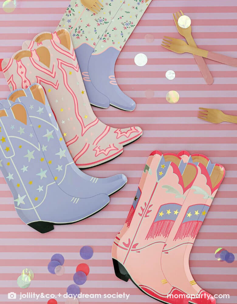 An overhead shot of Momopartys's 8" x 6" Pony Tales Large Boot Shaped Plates by Daydream Society with pink striped background and confetti and pink utensils around. Comes in a set of 8 cowgirl boots shaped plates in 4 different designs and colors, these plates feature pink and purple boots trimmed with gold and silver foil details are perfect for a Western cowgirl themed party or girl's horse/pony themed birthday celebration.