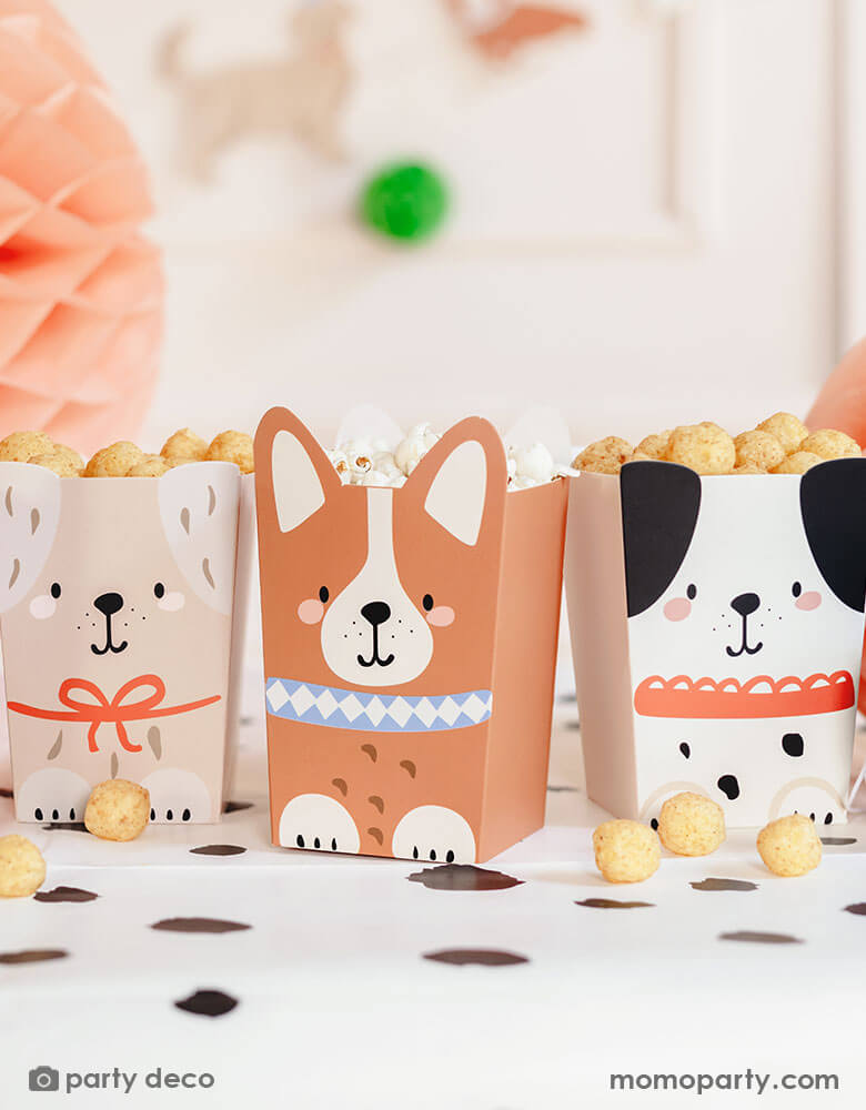 An adorable dog puppy themed birthday party table featuring Momopartys's Puppy Dog Party Snack Treat Boxes by Party Deco. These snack boxes come in 4 designs of different puppies with adorable dog design on it. They're filled with popcorn, chips and treats placed on the Dalmatian printed dot tablecloth underneath, with pastel honeycomb decorations around the table and a happy birthday banner in the back, this makes a cute scene for kid's dog themed birthday party celebration.