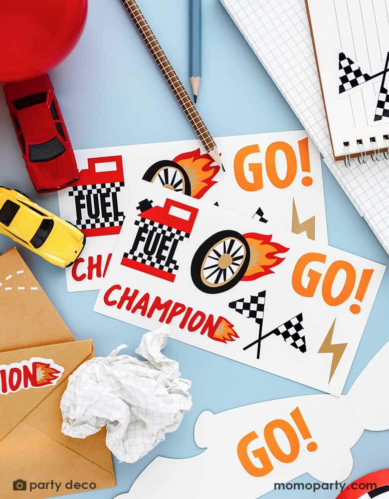 Two sets of Momopartys's race car stickers by Party Deco surrounded by some stationary and toy race cars, the notebook and the party invitations are adorned with these race car themed stickers, making it a perfect idea for kid's race car themed birthday invites.