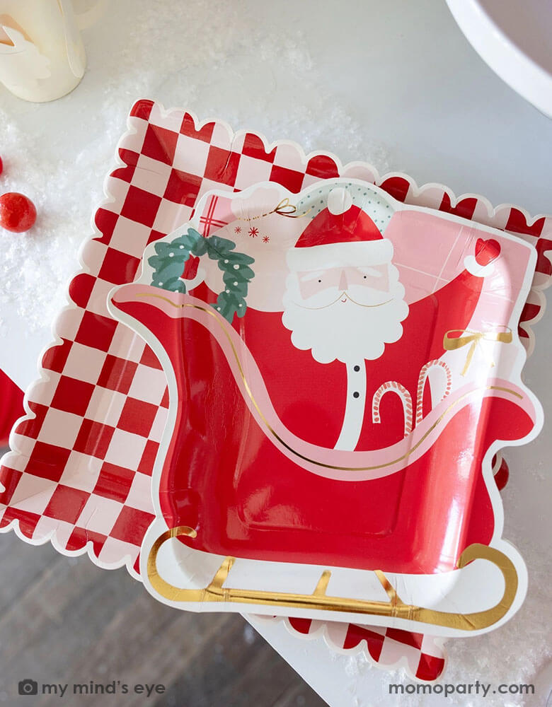 A table shot of Momopartys's 10" Pink and Red Checked Paper Plates and the Santa on a sleigh shaped plate by My Mind's Eye. These playful Santa inspired plates add a touch of fun to any table setting. Get ready to serve up some serious style with these quirky and eye-catching plates this Holiday season!