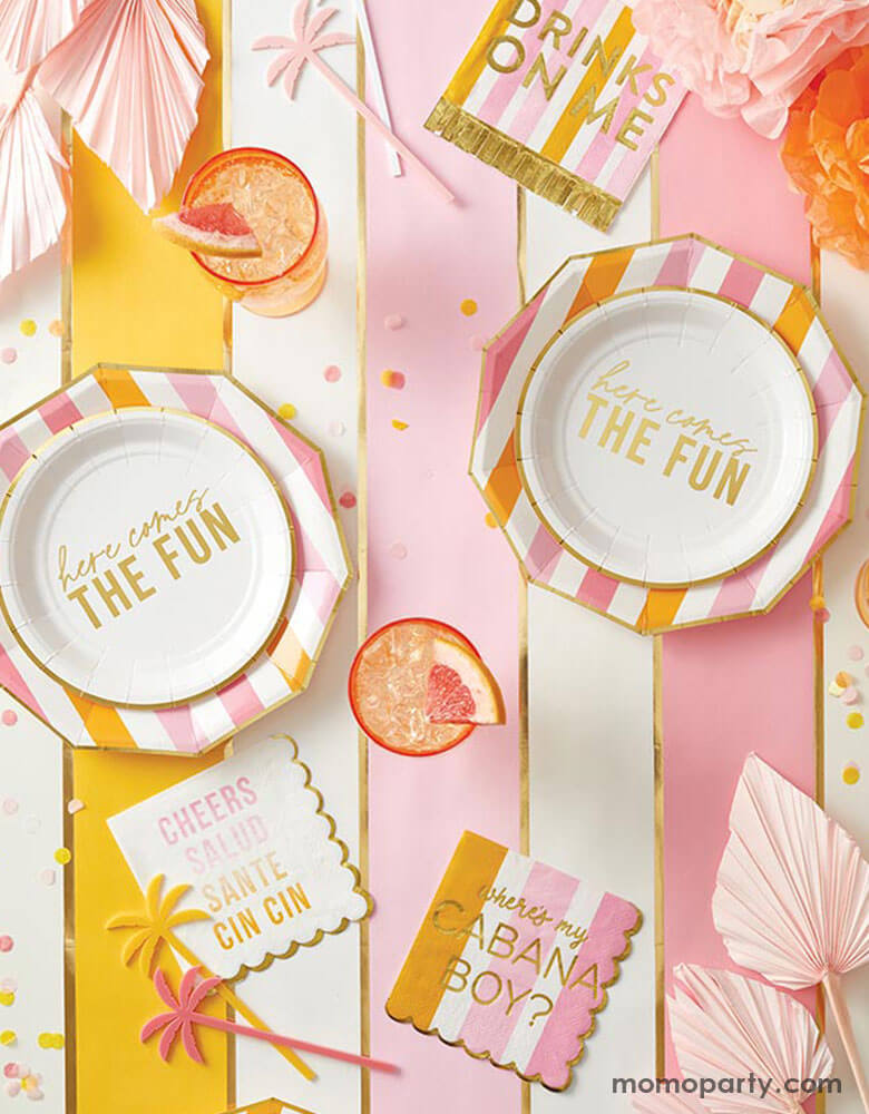 A festive pink and orange summer themed part table featuring Momopartys's here comes the fun party supplies including cheerful plates, napkins in pink and orange stripes, palm tree shaped stirrers, summer bouquets and refreshing summer drinks topped with tropical fruit - a perfect inspo for a fun and bright summer celebration in the sun!