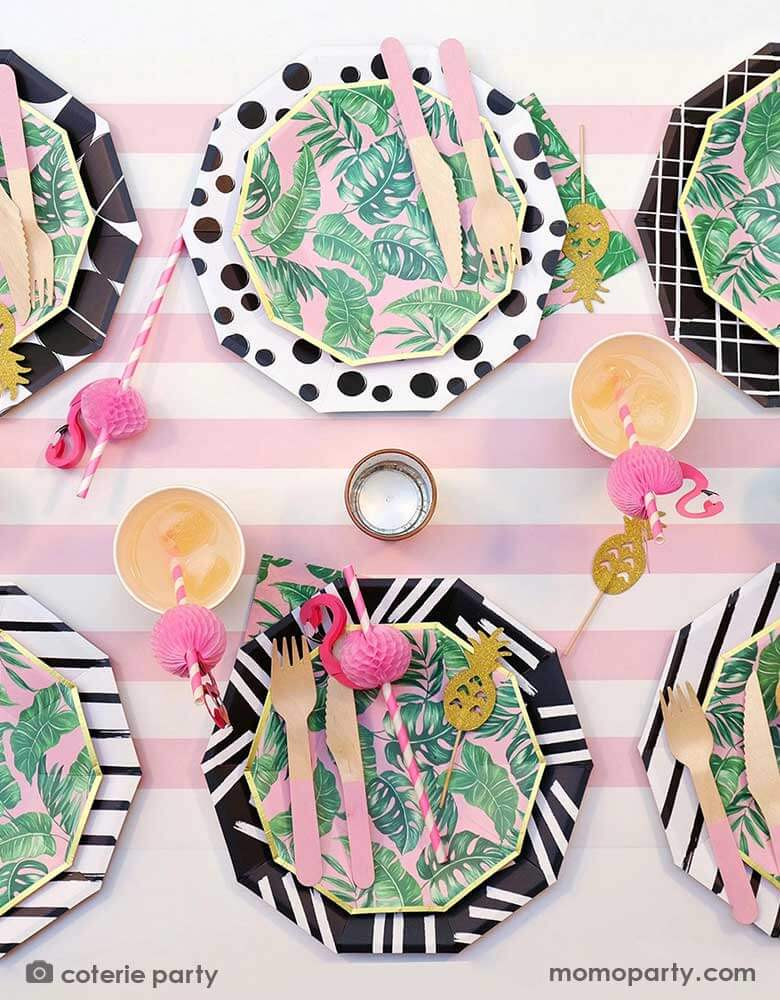 A modern summer tropical themed party tablescape features Momopartys's tropical party themed party supplies including palm leaf plates, napkins, pink wooden utensil set and flamingo honeycomb paper straws in the party cups. All these are on a pink striped table runner, making this a festive yet modern look for a summer party!