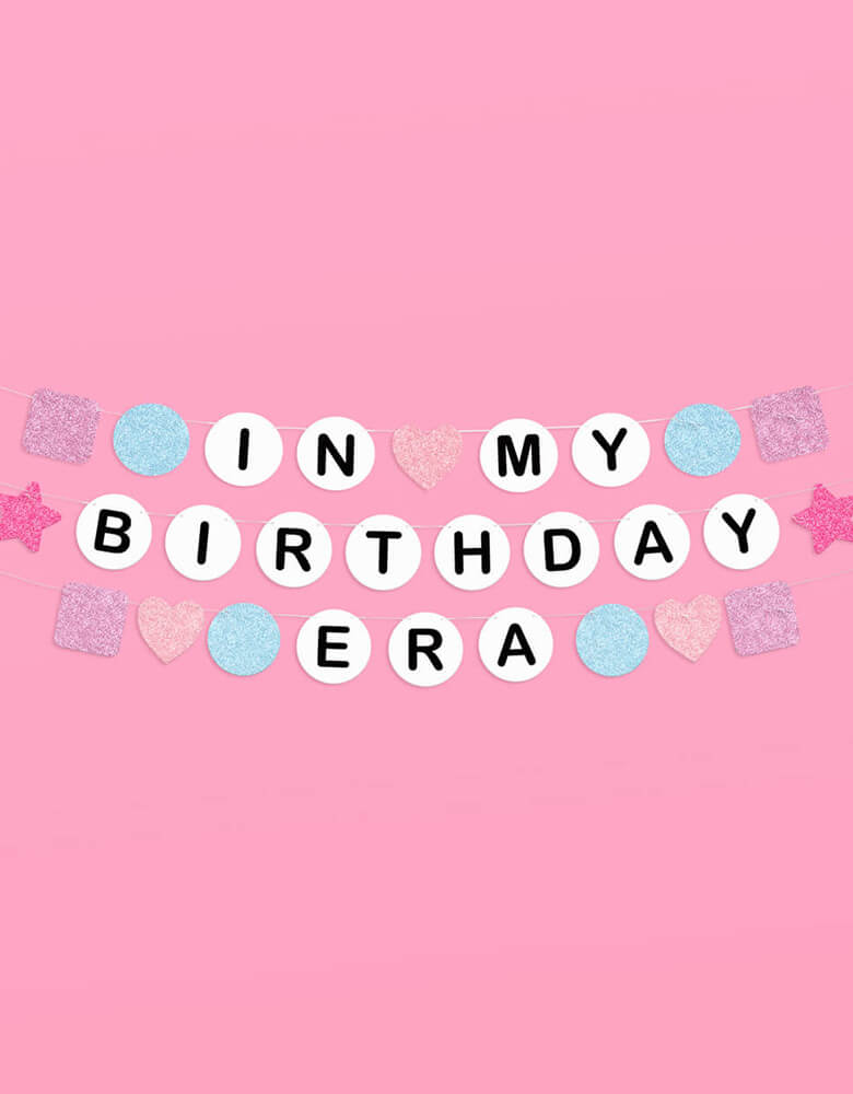 Momo Party's 5' Taylor Swift In My Birthday Era friendship bracelet inspired birthday party banner by Xo, Fetti. Made with paper with glittered pennants in purple, pink and blue, this fun birthday banner is perfect for any Swiftie for their special day!