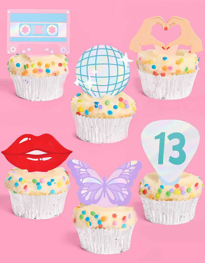 A few birthday cupcakes adorned with Momopartys's Era's Party Cupcake Toppers by Xo, Fetti. Comes in a set of 24, these Taylor Swift-themed dessert/cupcake toppers are with iconic designs including butterflies, red lips, disco balls, cassettes, guitar picks and heart hand symbols. They're perfect for to celebrate your Swiftie girl's special birthday.