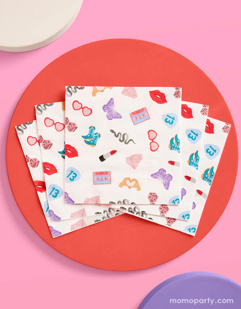Momo Party's 5" x 5" Taylor Swift Era's Party small napkins Xo, Fetti. Comes in a set of 25 napkins, these napkins have a Taylor Swift inspired motif featuring red lipstick, red lips, butterflies, cowgirl boots, snakes, cassette tapes, guitar picks, heart hand symbols, and heart shaped sunglasses. They're perfect for the party table celebrating your Swiftie girl's special day.