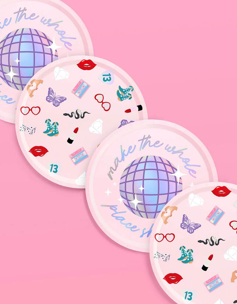 Momo Party's 9" x 9" Taylor Swift Era's Party Paper Plates by Xo, Fetti. Comes in a set of 24 paper plates in two different designs, a disco ball and a Taylor Swift inspired motif featuring red lipstick, red lips, butterflies, cowgirl boots, snakes, cassette tapes, guitar picks, heart hand symbols, and heart shaped sunglasses. They're perfect for the party table celebrating your Swiftie girl's special day.