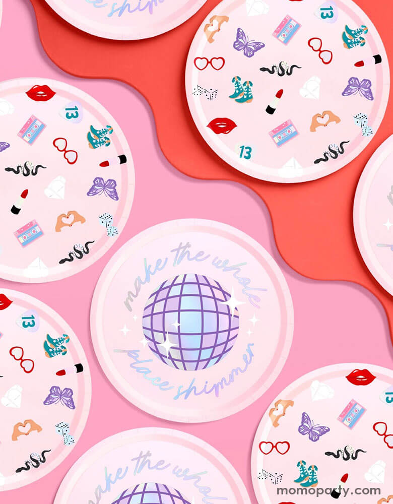 Momo Party's 9" x 9" Taylor Swift Era's Party pink paper plates by Xo, Fetti. Comes in a set of 24 paper plates in two different designs, a disco ball and a Taylor Swift inspired motif featuring red lipstick, red lips, butterflies, cowgirl boots, snakes, cassette tapes, guitar picks, heart hand symbols, and heart shaped sunglasses. They're perfect for the party table celebrating your Swiftie girl's special day.