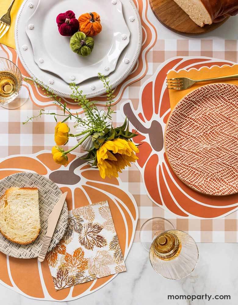 A beautiful fall tablescape featuring Momopartys's fall themed tableware including the pumpkin shaped paper placemats, maple leaf napkins and brown gingham table runner, with fall flower bouquet and pumpkin decorations, this makes a great inspo for a gorgeous fall party or Thanksgiving gathering table decoration idea.