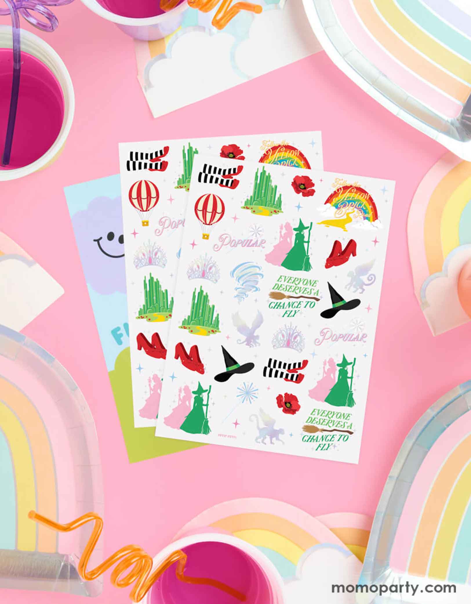 Momo Party's Emerald City Wicked Witch Temporary Tattoos by Xo, Fetti. Featuring green witch hats, broomsticks, and magical icons inspired by the Wizard of Oz. On the table around the tattoo sheets there are some rainbow shaped plates and party cups with pink juice, making it perfect for a Wicked themed birthday party celebration!